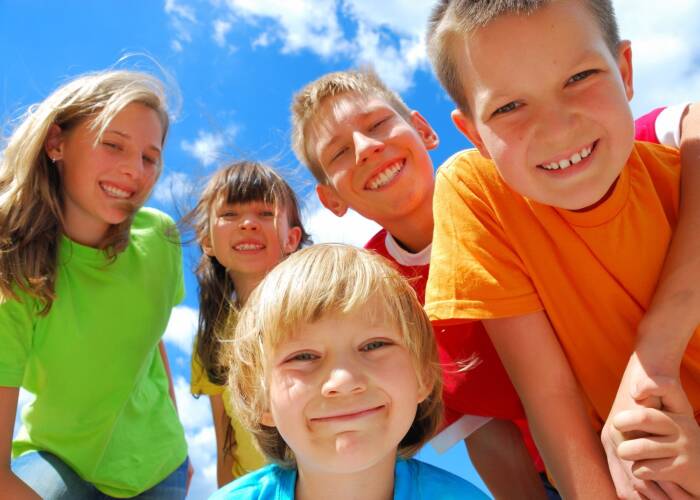 Portrait of five smiling children taken from low perspective upward as they bend over toward the camera. Blue sky and clouds background.